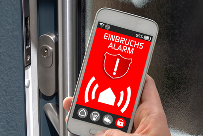 Eine geöffnete Haustür und ein Handy im Vordergrund mit der Meldung Einbruchsalarm.